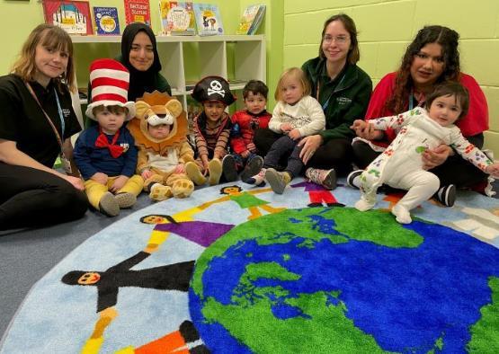 Nursery staff and children sat down inside family study room at university with books on shelves