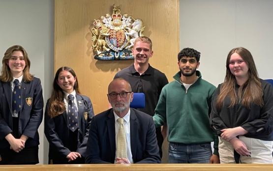 A group of school students stood behind a judge who is sat down in a courtroom