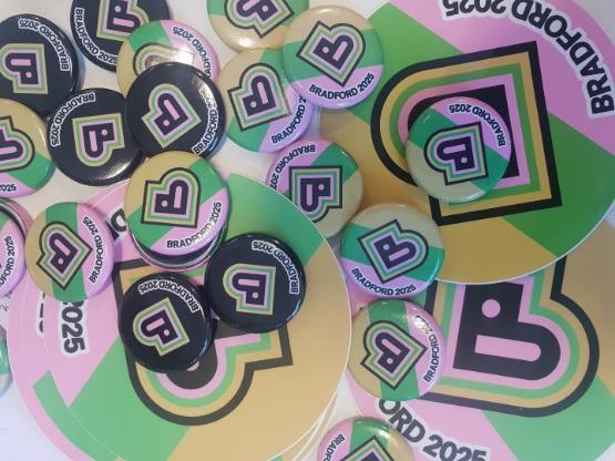 A selection of small Bradford 2025 badges which are coloured pink, green, yellow and black