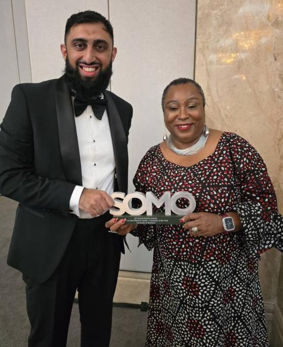 Two members of university staff in formal wear hold an award won at a ceremony