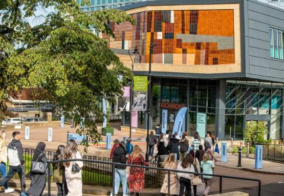 A group of people outside walking towards the main entrance of the Richmond building at university which is in front of them