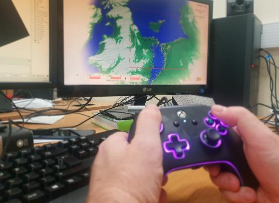 Someone holding an X-box controller with a computer screen in the background