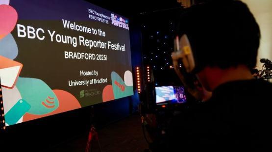 a TV camera is filming a large screen advertising a festival