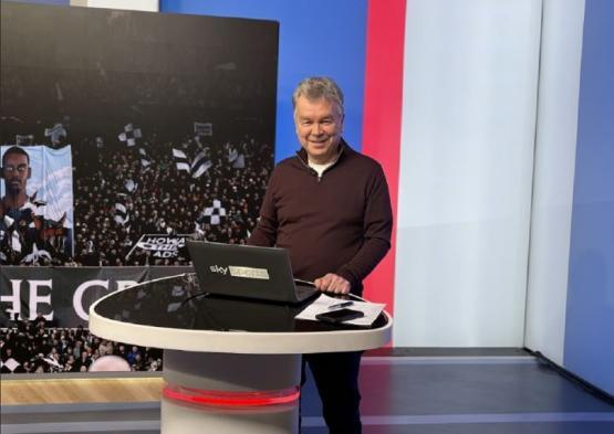 Person stood up behind a small table with laptop on it in a TV studio