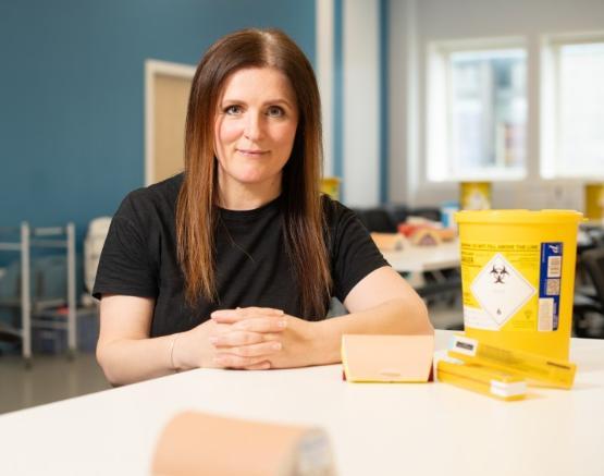 A person sat at a table which has drug equipment including a small bucket in front of them