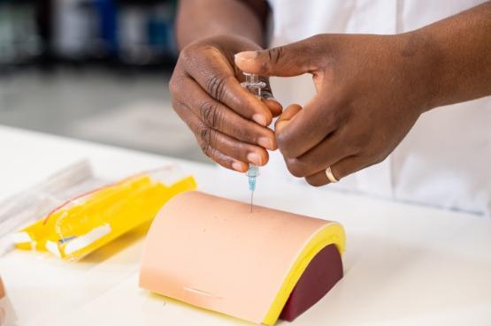 A close-up picture of someones hands who is holding and placing a needle into a small oval shaped object on a table