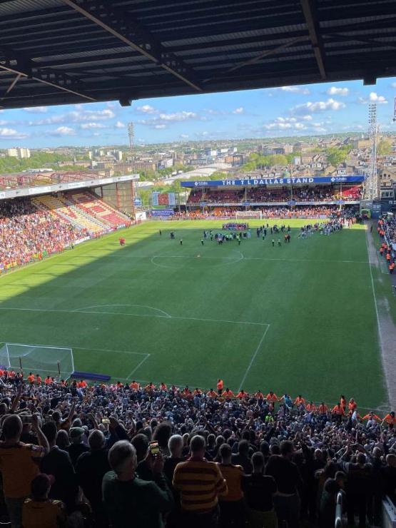 A view of a large crowd at a football match with people celebrating on the pitch