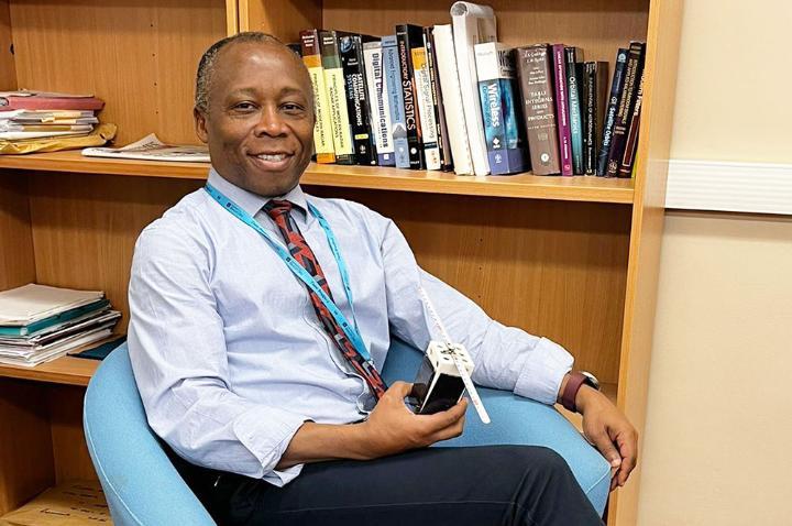 Prof Ifiok Otung seated, holding the PocketQube satellite protoype