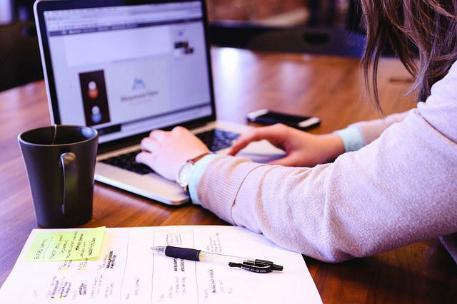 A person working on a laptop with a pad and hot drink next to them