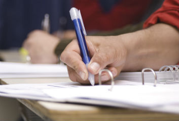 A student writing notes on paper in a ring binder folder.