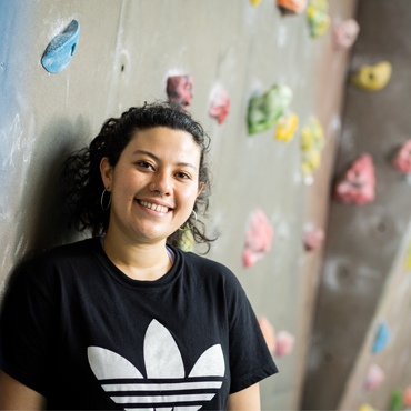 A student smiling stood in front of the on-campus climbing wall