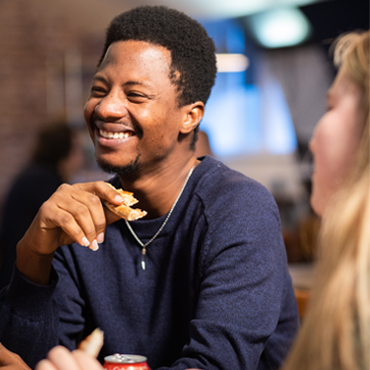 A student smiling and eating pizza with a friend