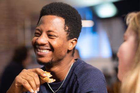 Student eating pizza with a friend smiling