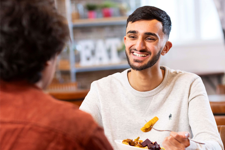 A student smiling whilst eating a meal with a friend