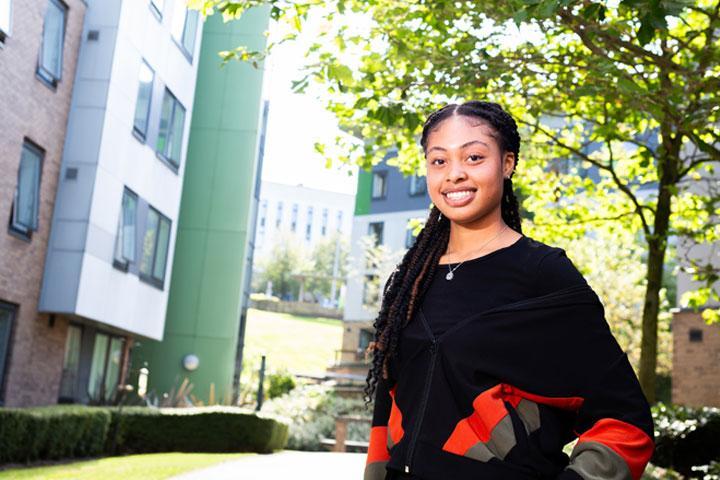 A student standing outside the accommodation at The Green, smiling at the camera.