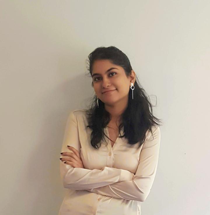 Sneha with arms folded in front of a white wall. 