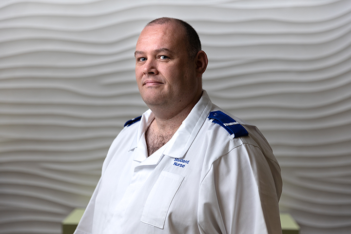 Student nurse in uniform stood in front of a white textured wall