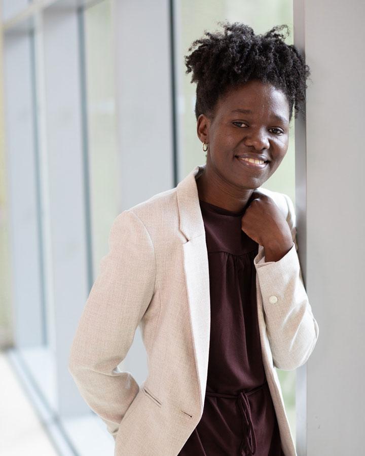 A smartly dressed person in a white jacket leaning on a window and smiling at the camera.