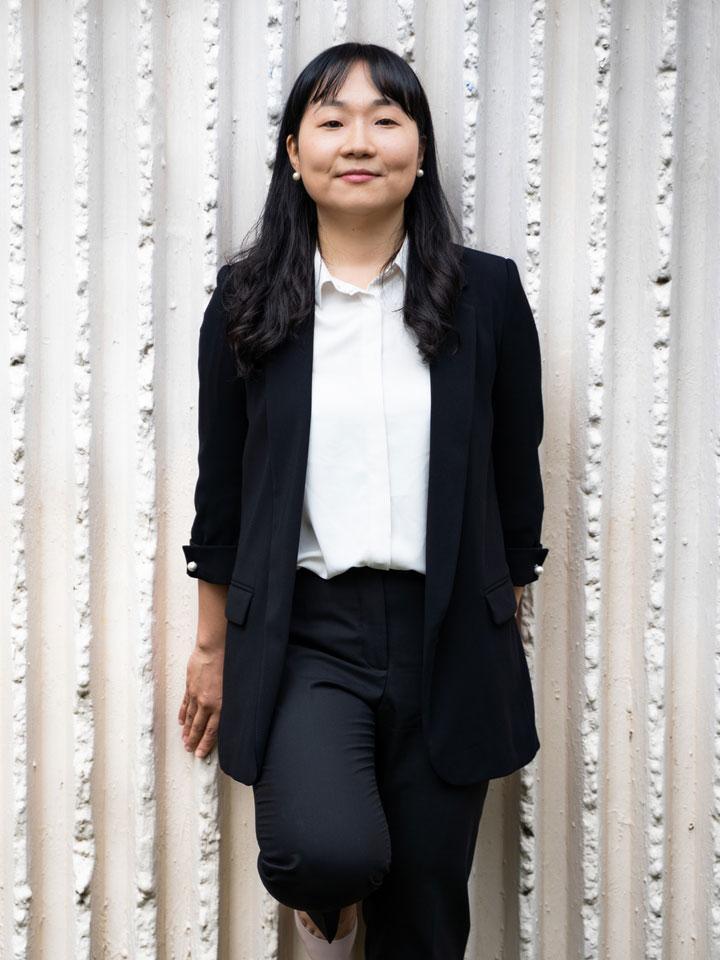 A smartly dressed person facing the camera and leaning on a white wall.