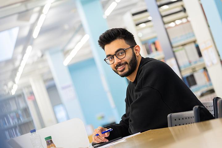 A student sat at a desk smiling at the camera