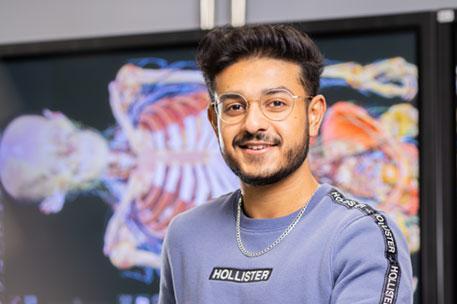 A student smiling at the camera with a digital skeleton in the background.