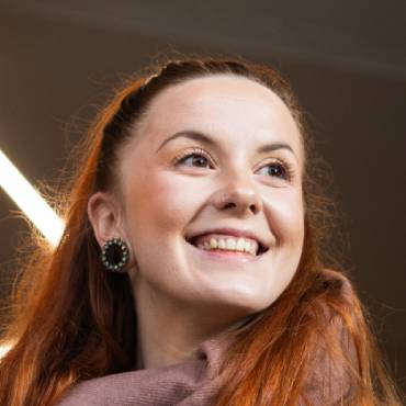 A woman looks to the right of the camera while smiling with bright strip lights behind her.