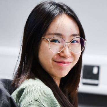 A student with long black hair and glasses smiles at the camera.