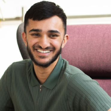 A student with a green top and short, dark hair smiles at the right of the camera.