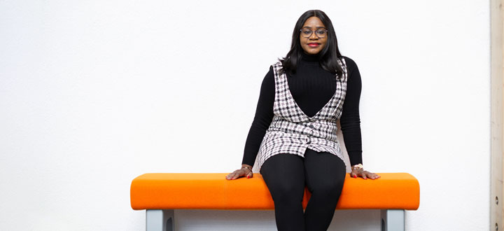 A person sitting on a bright orange bench against a white wall in a brightly lit room.