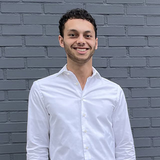 A smartly dressed person standing in front of a brick wall.