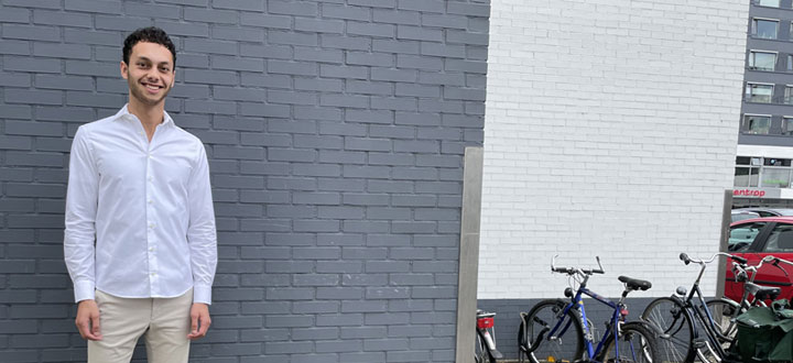 A person wearing a white shirt standing in front of a brick wall. There are some bicycles standing in the background.