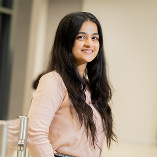 Student leaning against a glass bannister smiling at the camera