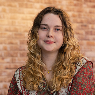 A student sitting in front of a brick background smiling at the camera