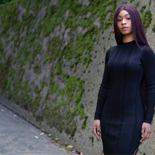 Female student wearing a black dress standing in front of a moss-covered stone wall